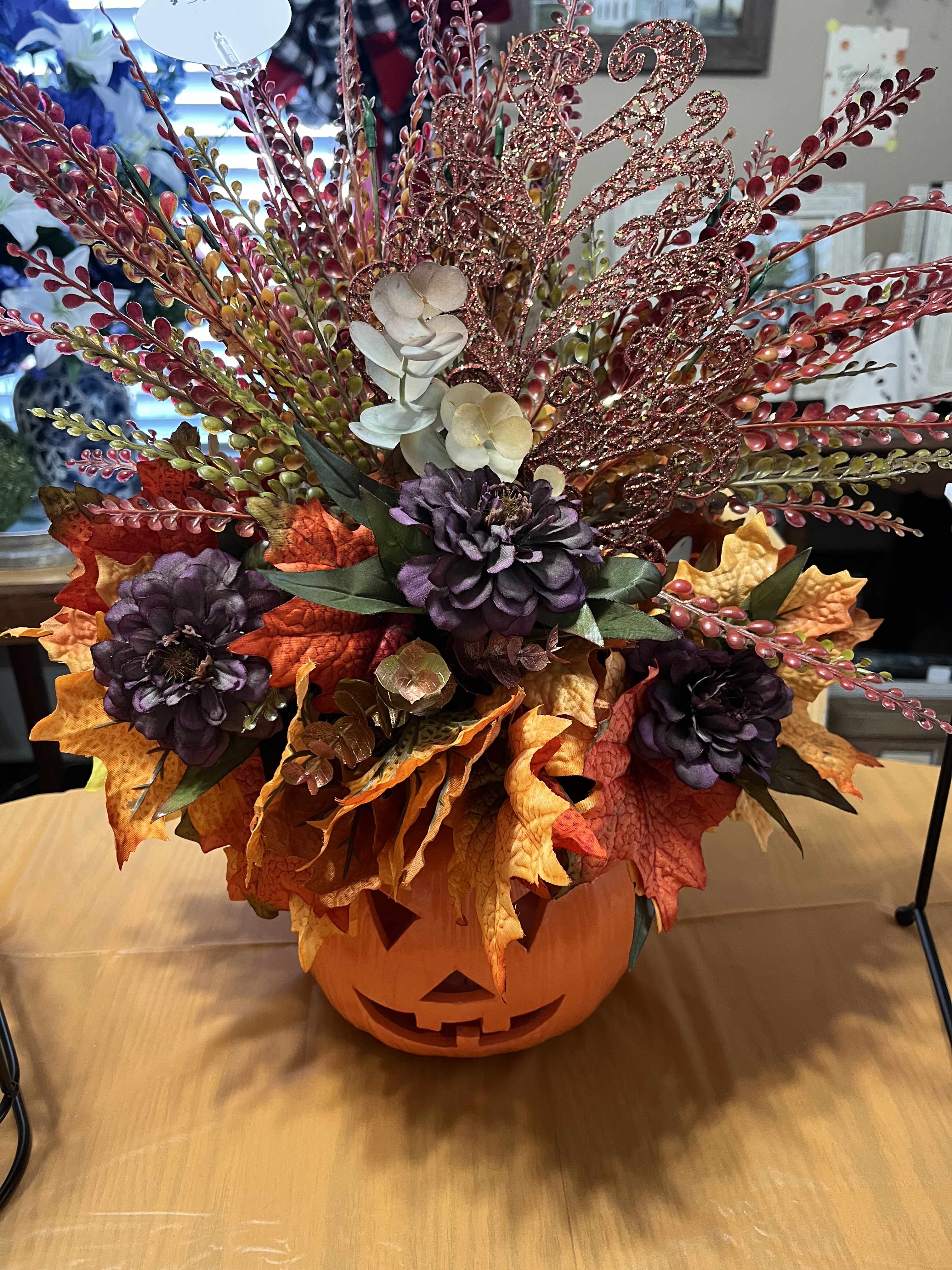 Halloween floral arrangement in a jack-o'-lantern container with autumn leaves