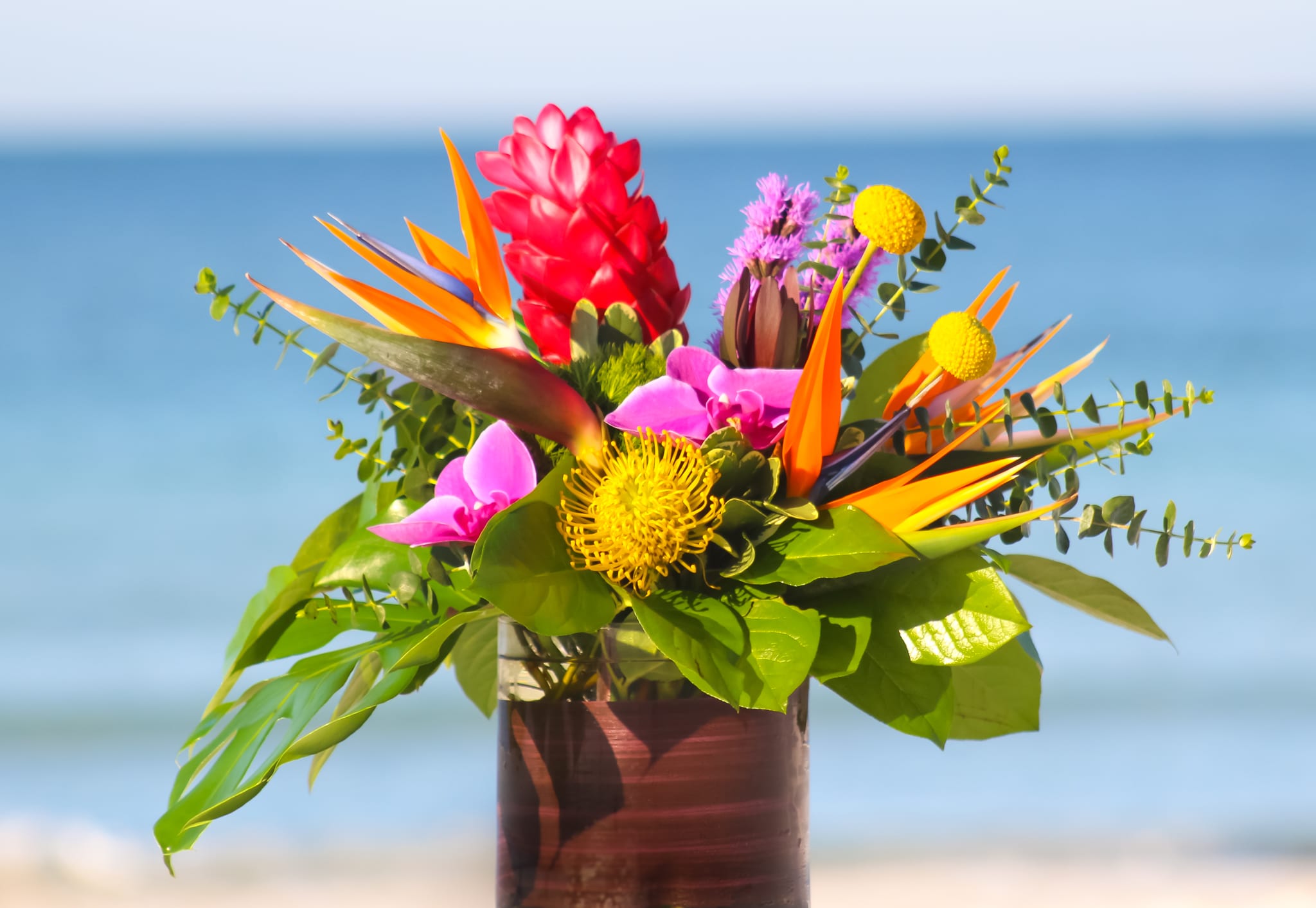 Tropical bouquet with bird of paradise, pink blooms, and yellow pincushion flowers in a vase
