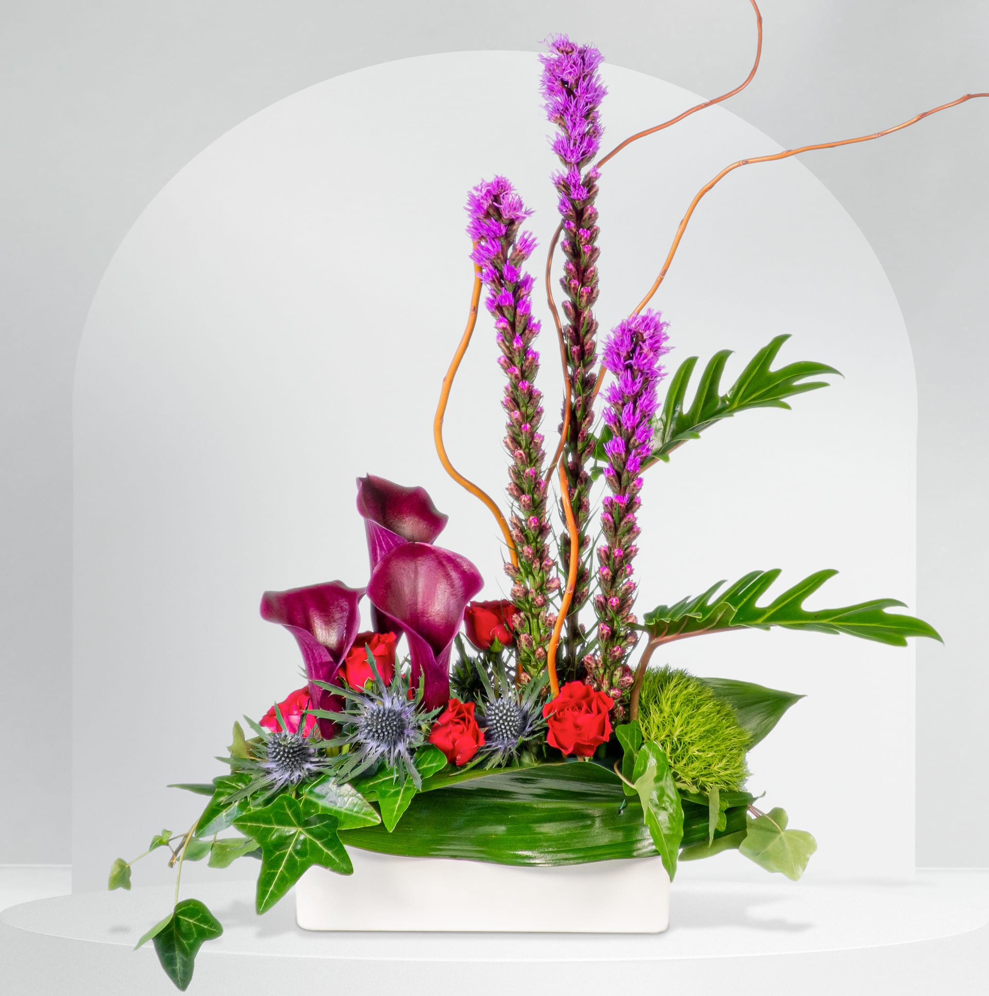 Purple calla lilies and red roses in a white rectangular vase