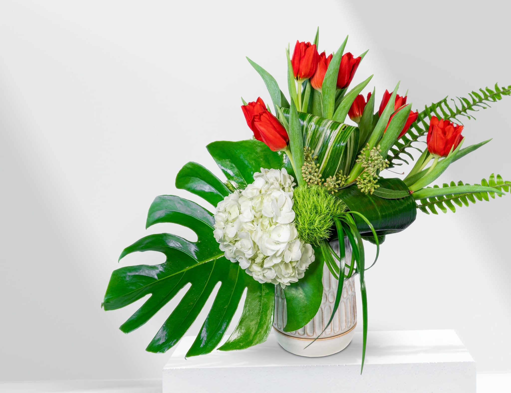 Red tulips and white hydrangea in a ceramic vase with large tropical leaves