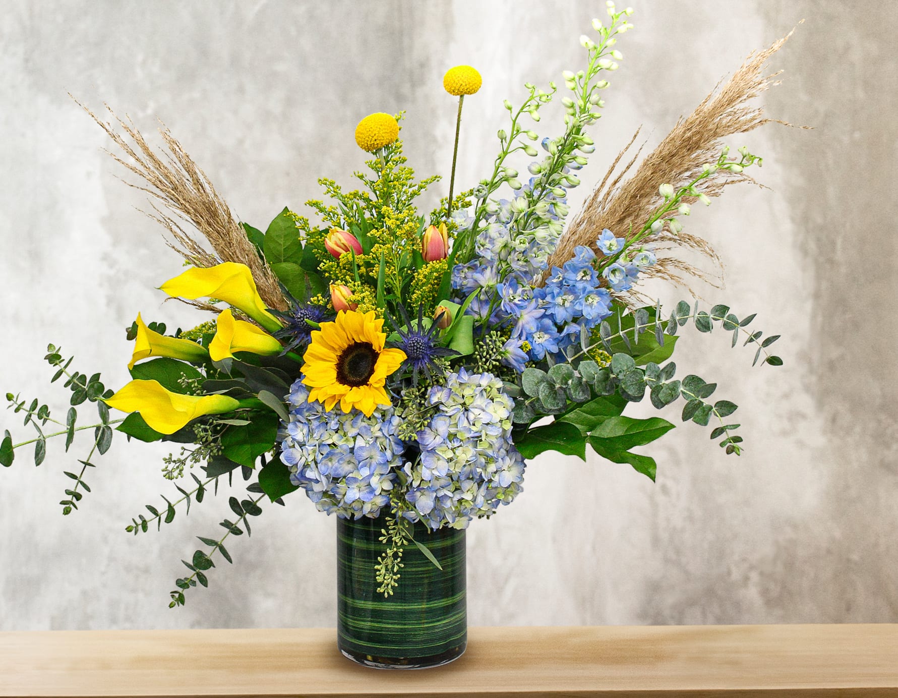 Mixed bouquet with sunflowers, calla lilies, and blue flowers in a glass vase