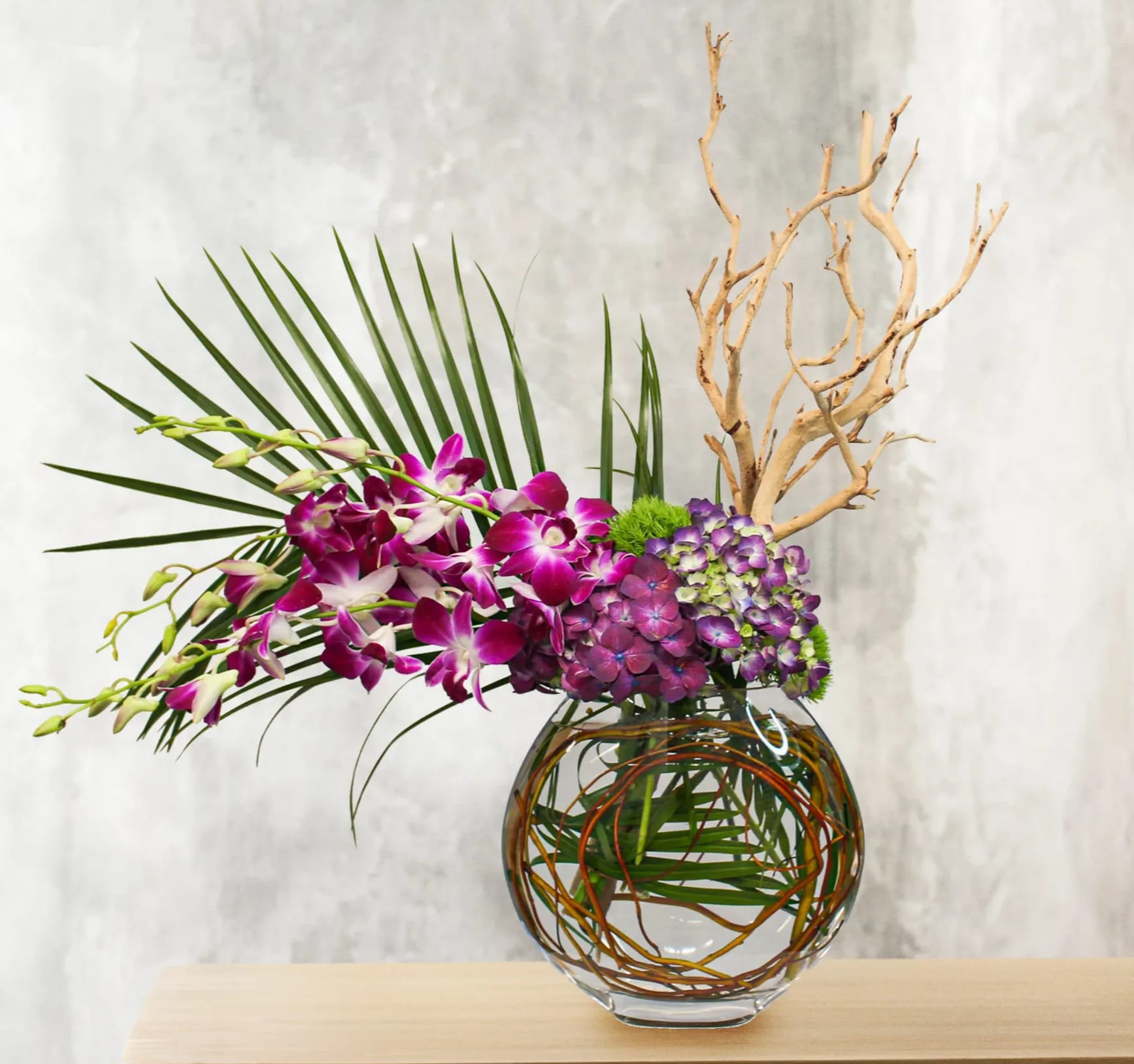 Purple orchids and hydrangeas in a glass vase with palm fronds and branches