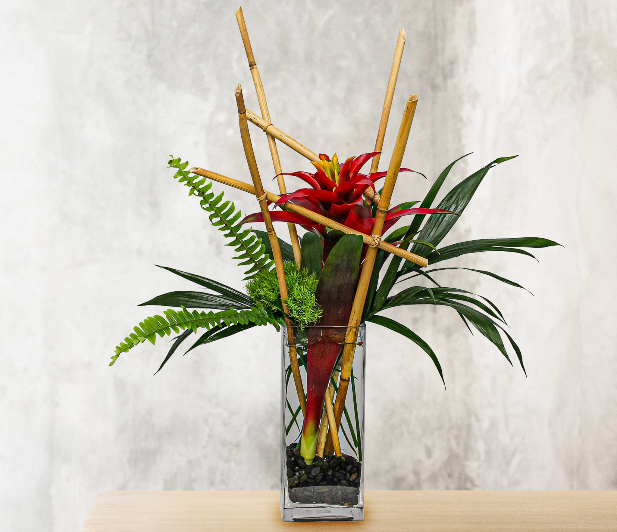 Red tropical flower arrangement in a tall glass vase with bamboo accents