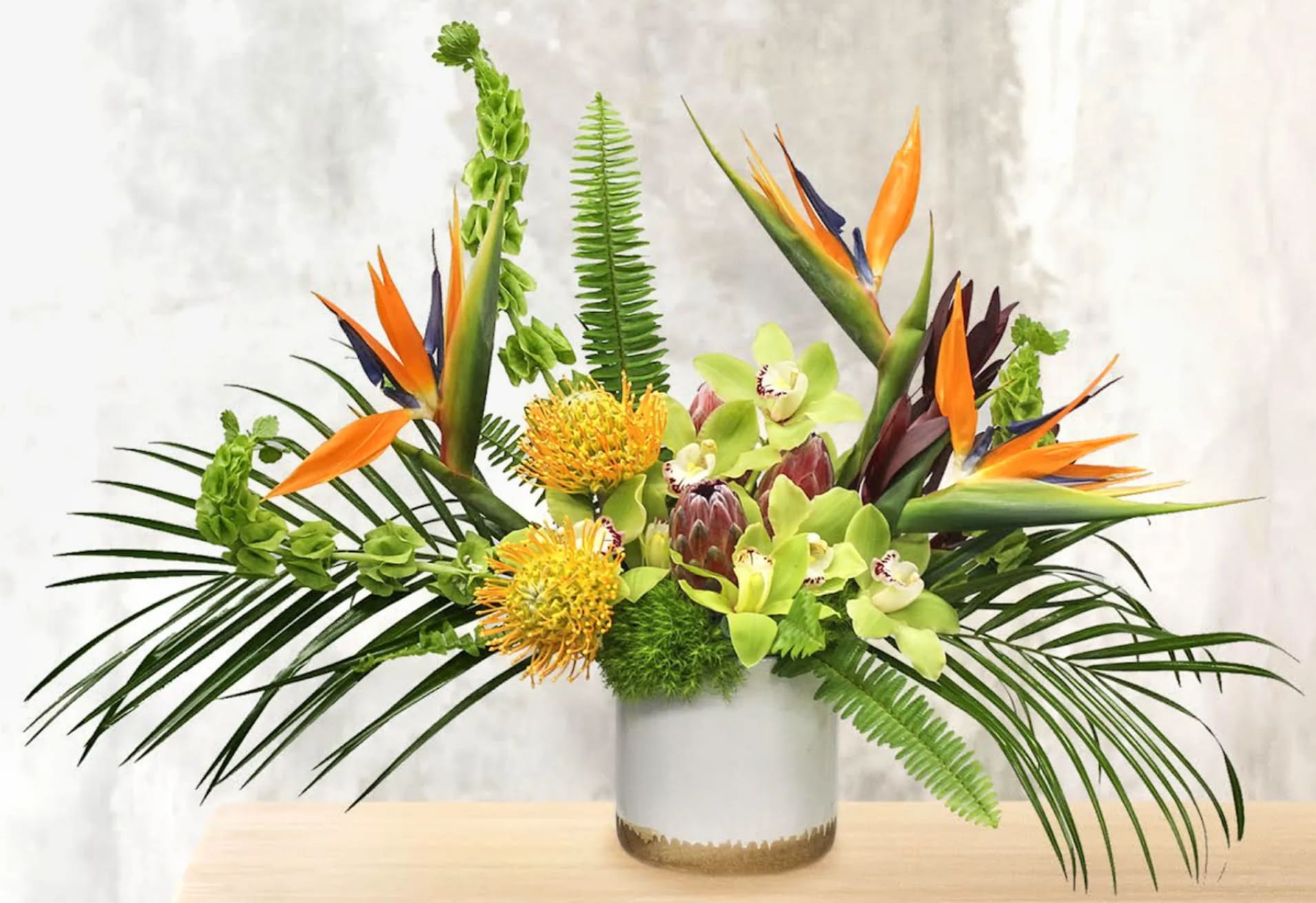 Tropical flower arrangement with orange bird-of-paradise and green orchids in a white vase