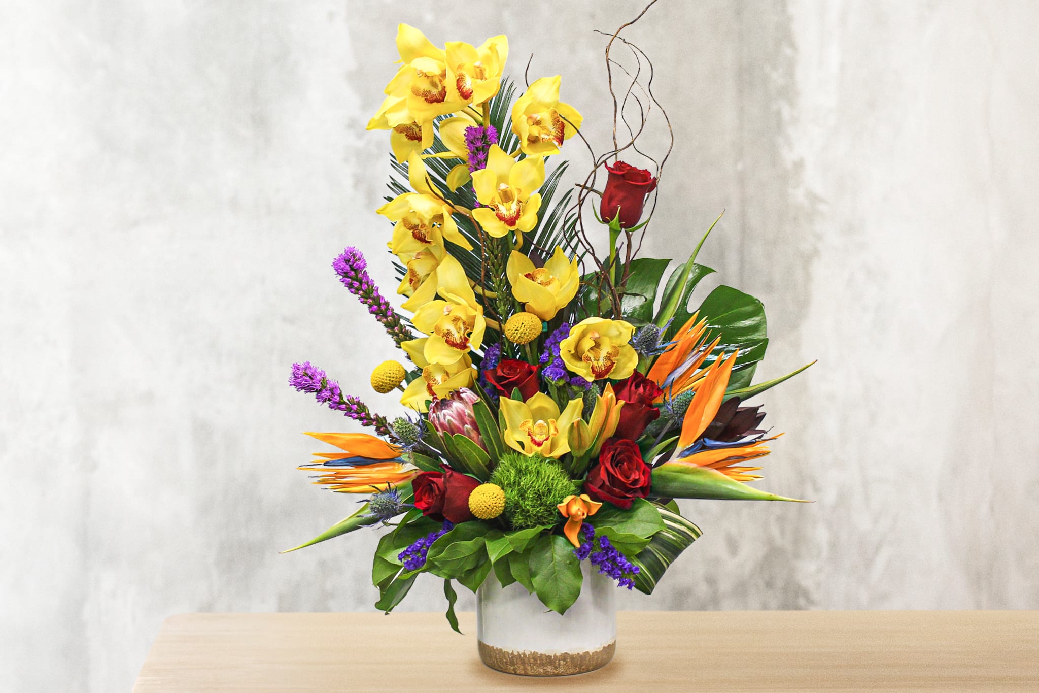Tall tropical bouquet with yellow orchids, red roses, and orange bird-of-paradise in a glass vase