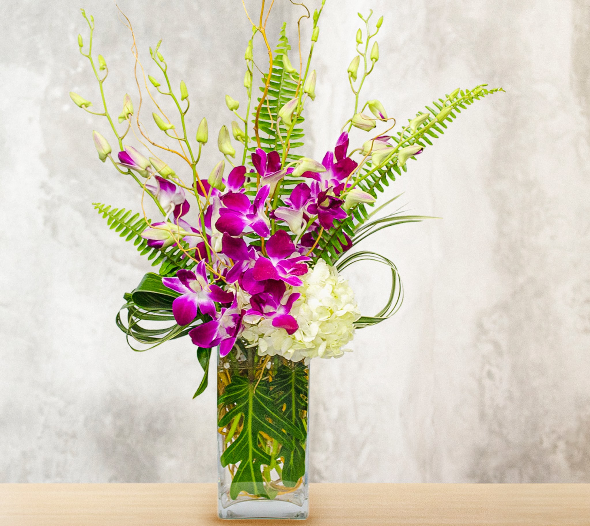 Purple orchids and white hydrangea in a clear rectangular vase