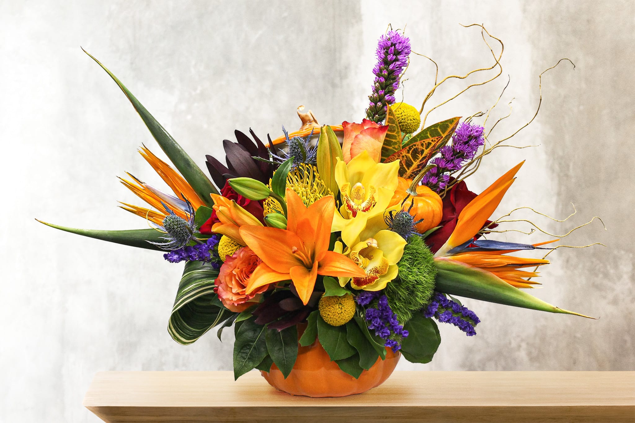 Tropical Pumpkin Centerpiece  - This unique tropical design includes, birds of paradise, orange lilies, roses, liatris, safari sunset, cymbidium orchids, pin cushion protea, dianthus green trick, crespedia, statice, thistle, and lush tropical foliage 