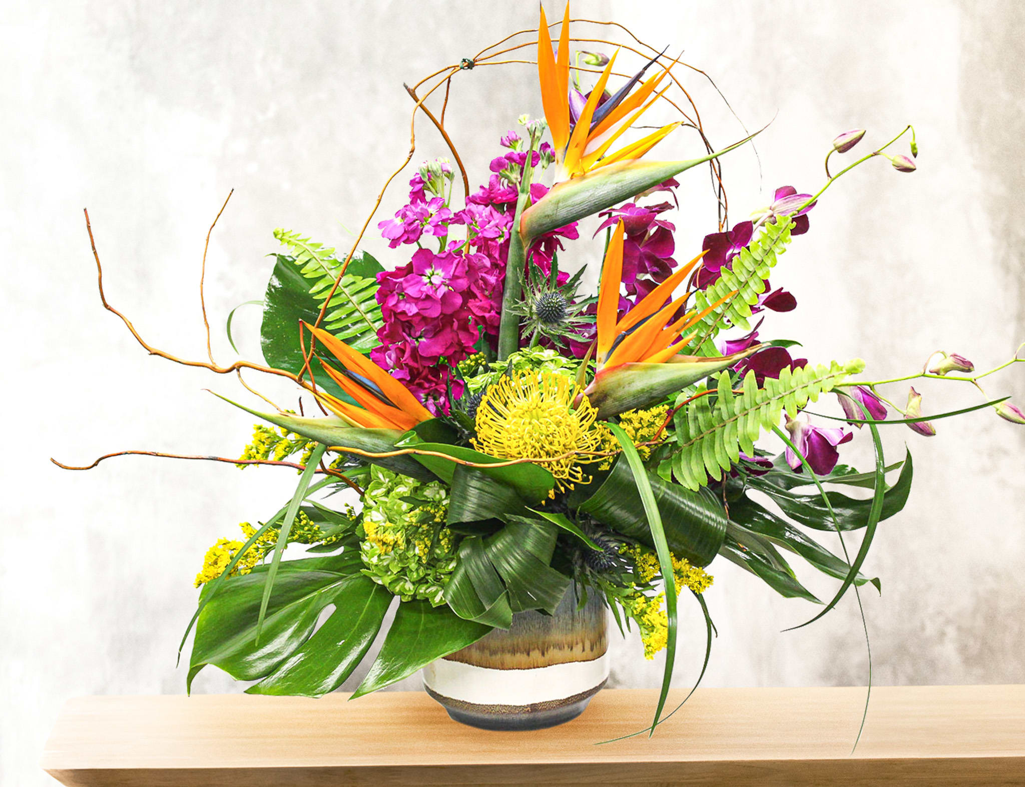 Tropical floral arrangement with orange bird-of-paradise and purple orchids in a vase