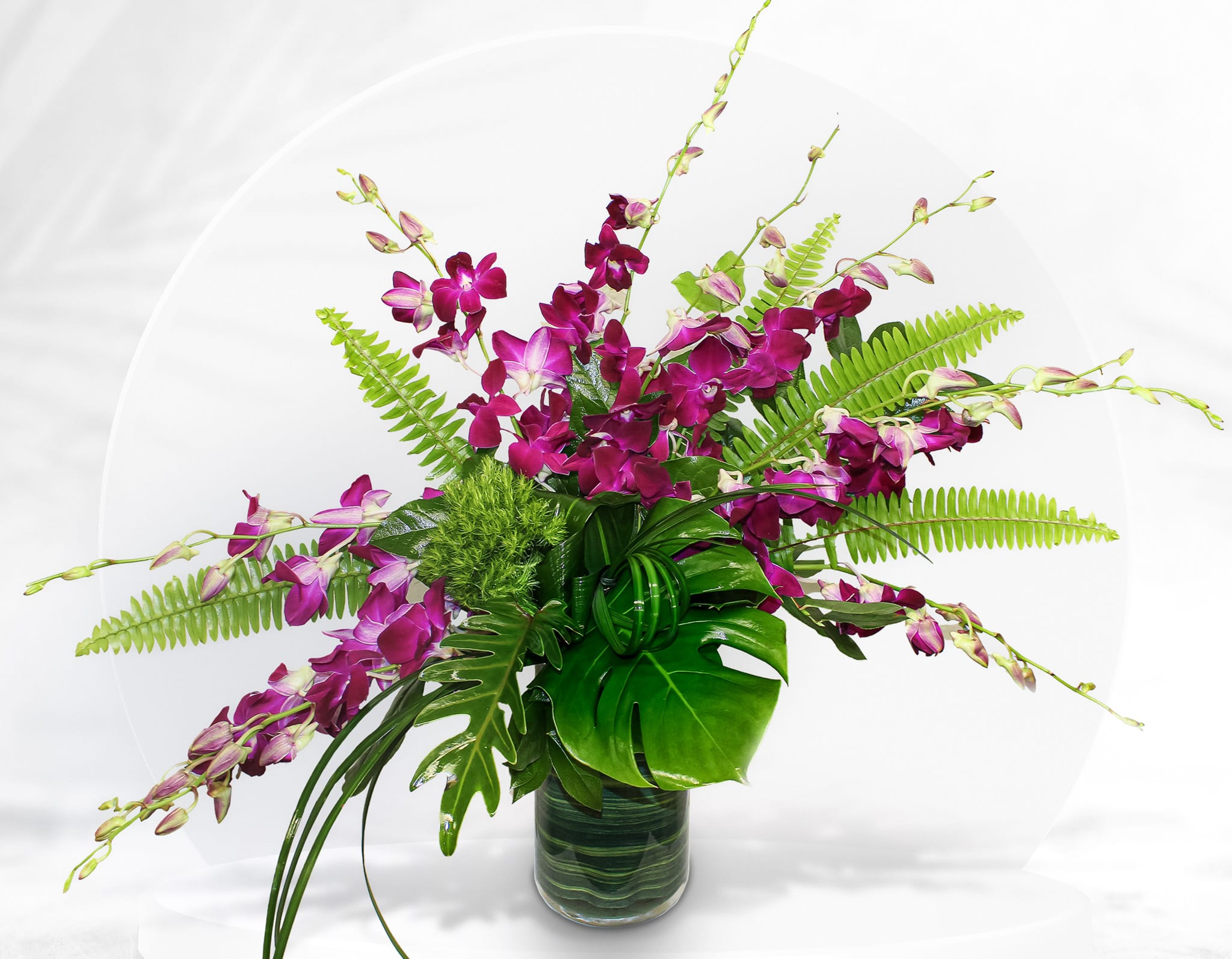 Purple orchid arrangement in a glass vase with tropical foliage