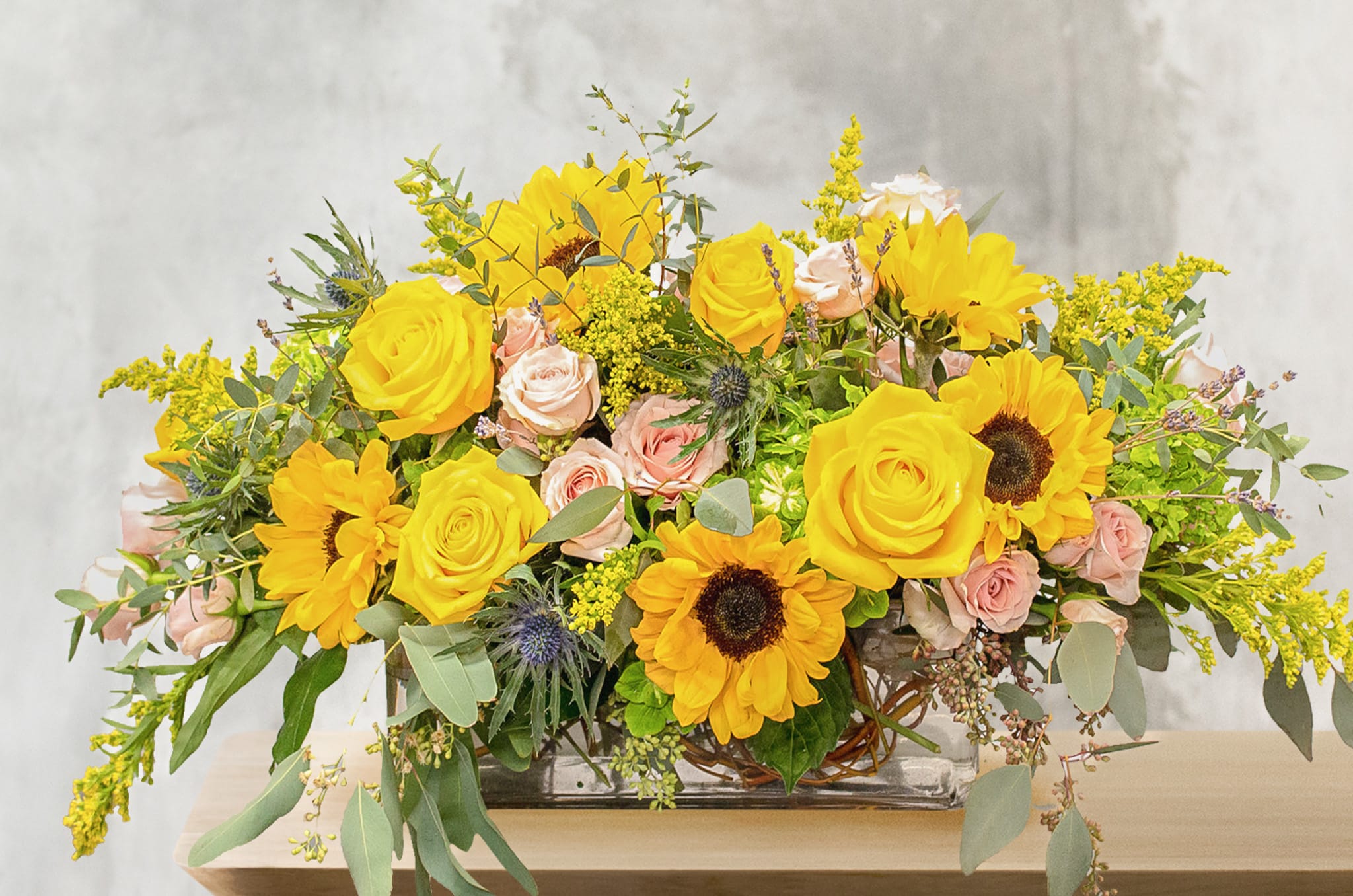 Yellow sunflowers and roses arranged in a glass vase