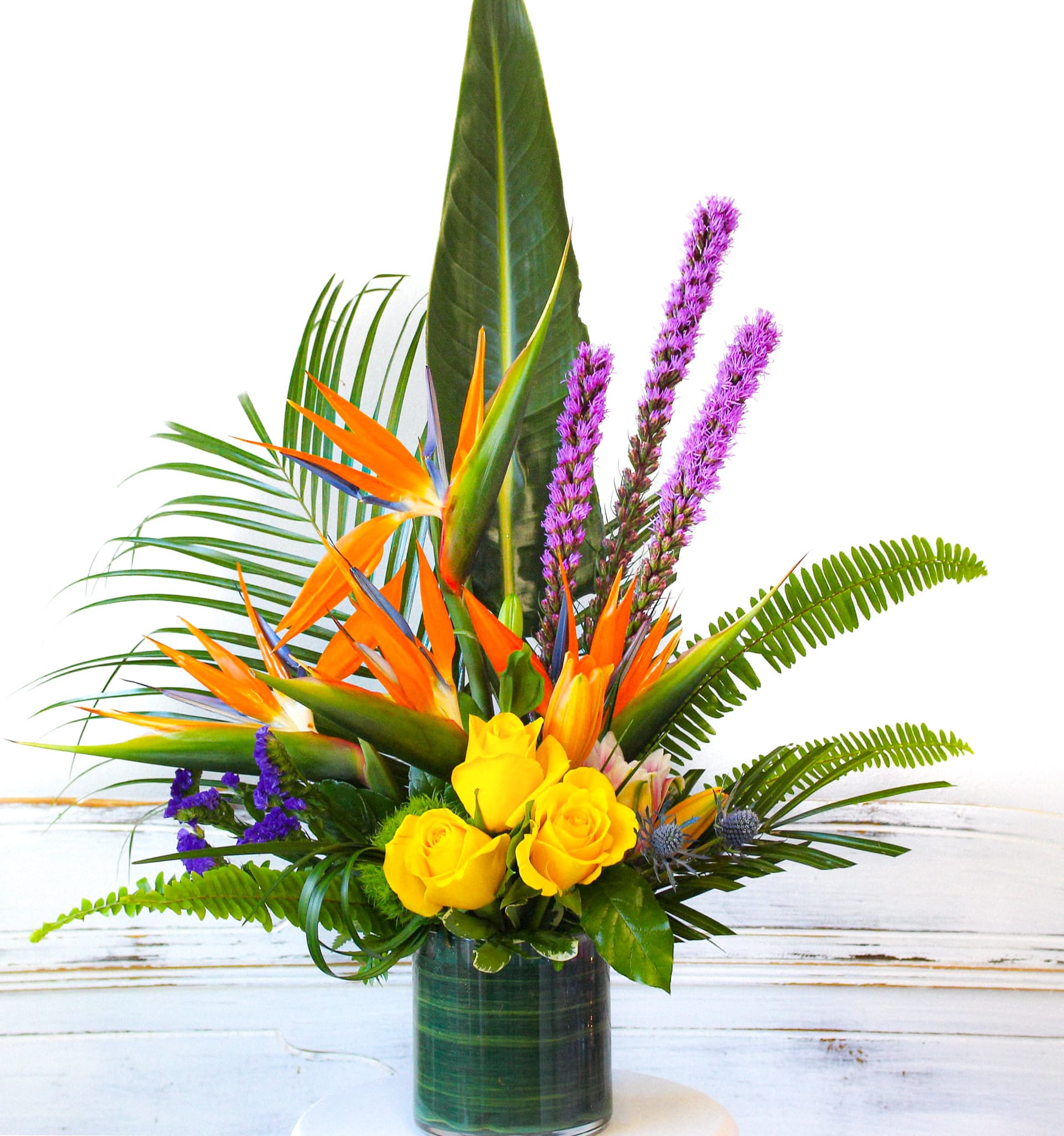 Tropical arrangement with yellow roses and orange bird-of-paradise in a glass vase