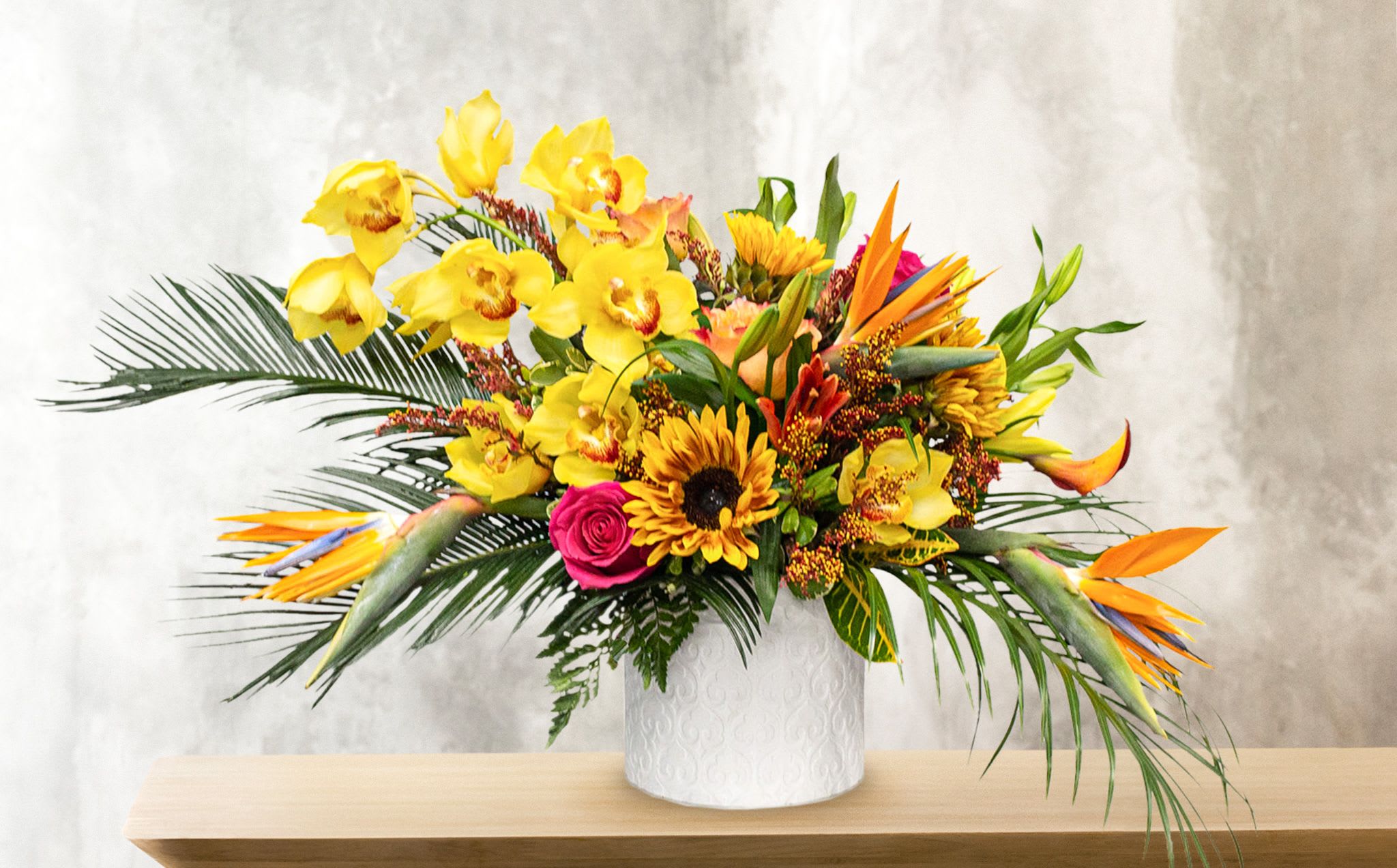 Tropical bouquet with yellow orchids, sunflowers, and bird-of-paradise in a white vase