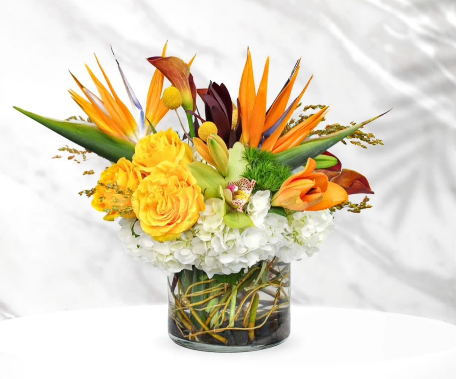 Tropical bouquet with orange bird of paradise and yellow roses in a glass vase
