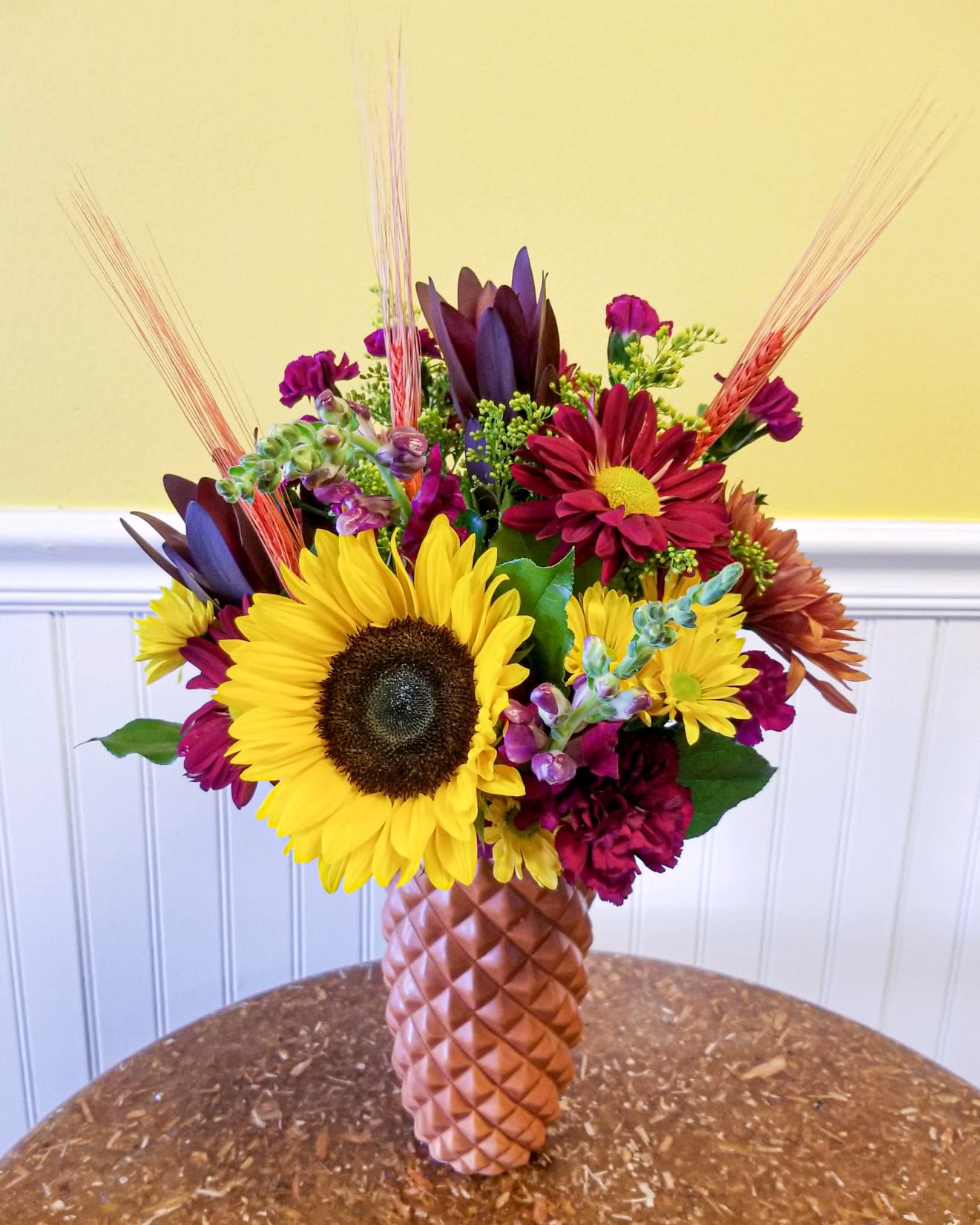 Mixed bouquet with sunflowers and burgundy blooms in a textured vase