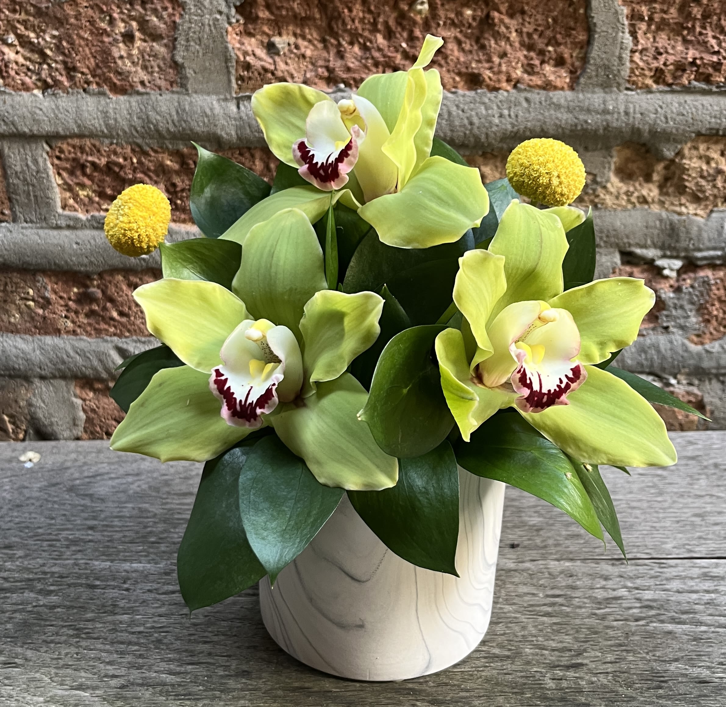 Green orchid arrangement in a white vase with yellow accents
