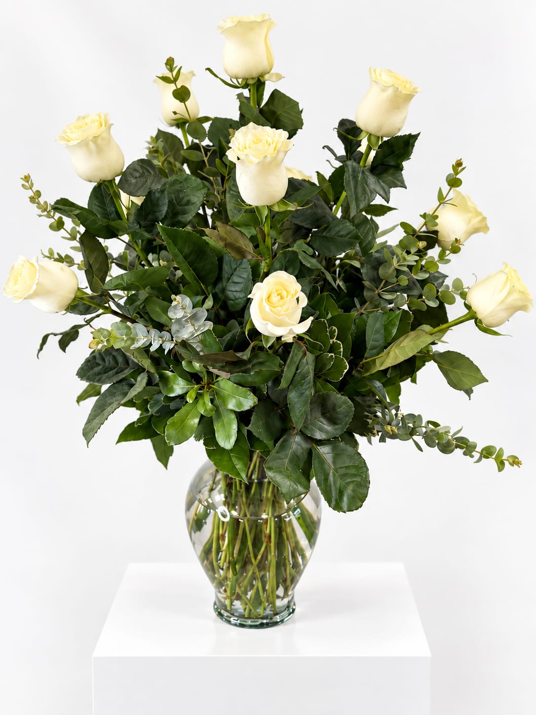 White roses in a clear glass vase with dark greenery