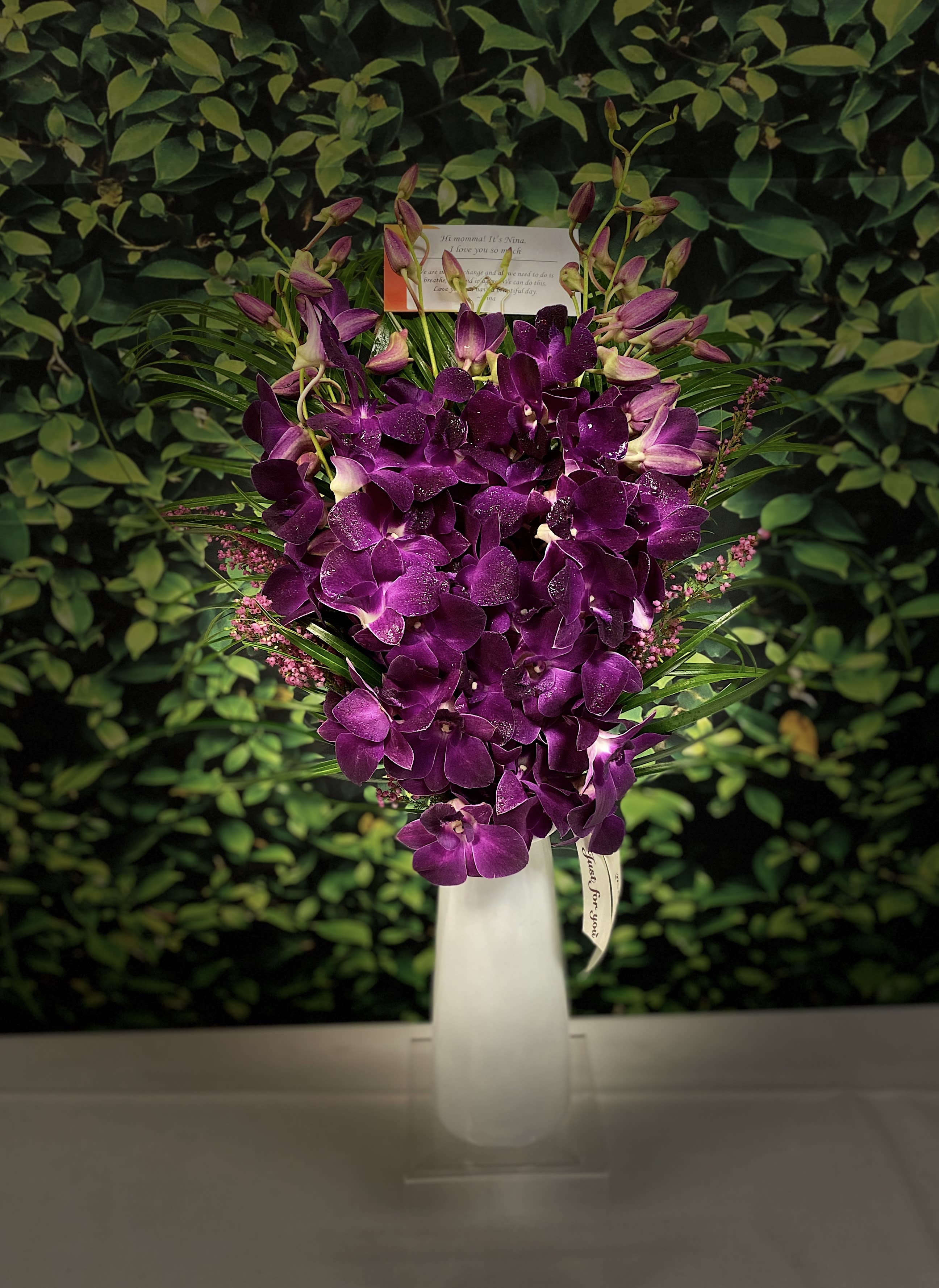 Purple orchid arrangement in a tall white vase