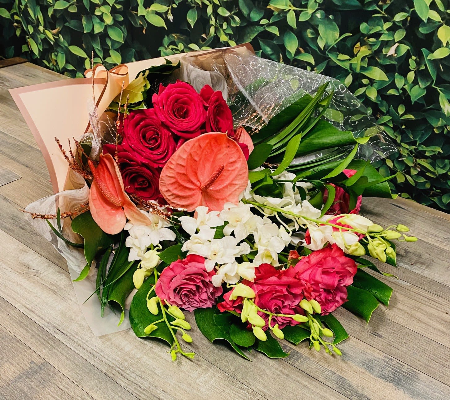 Bouquet of red roses, pink anthuriums, and white orchids with green leaves