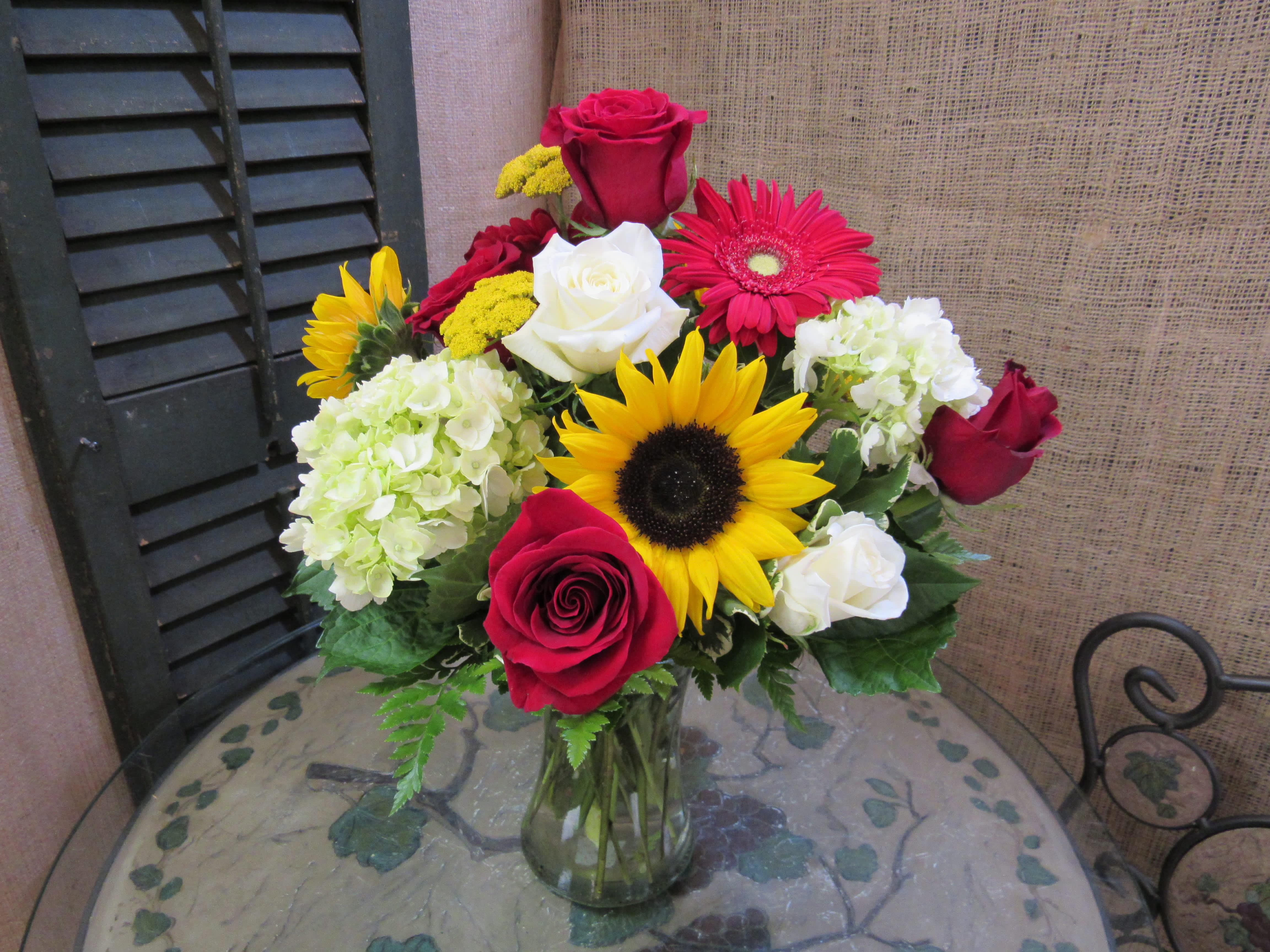 Mixed bouquet of roses, sunflowers, gerbera daisies, and hydrangeas in a glass vase
