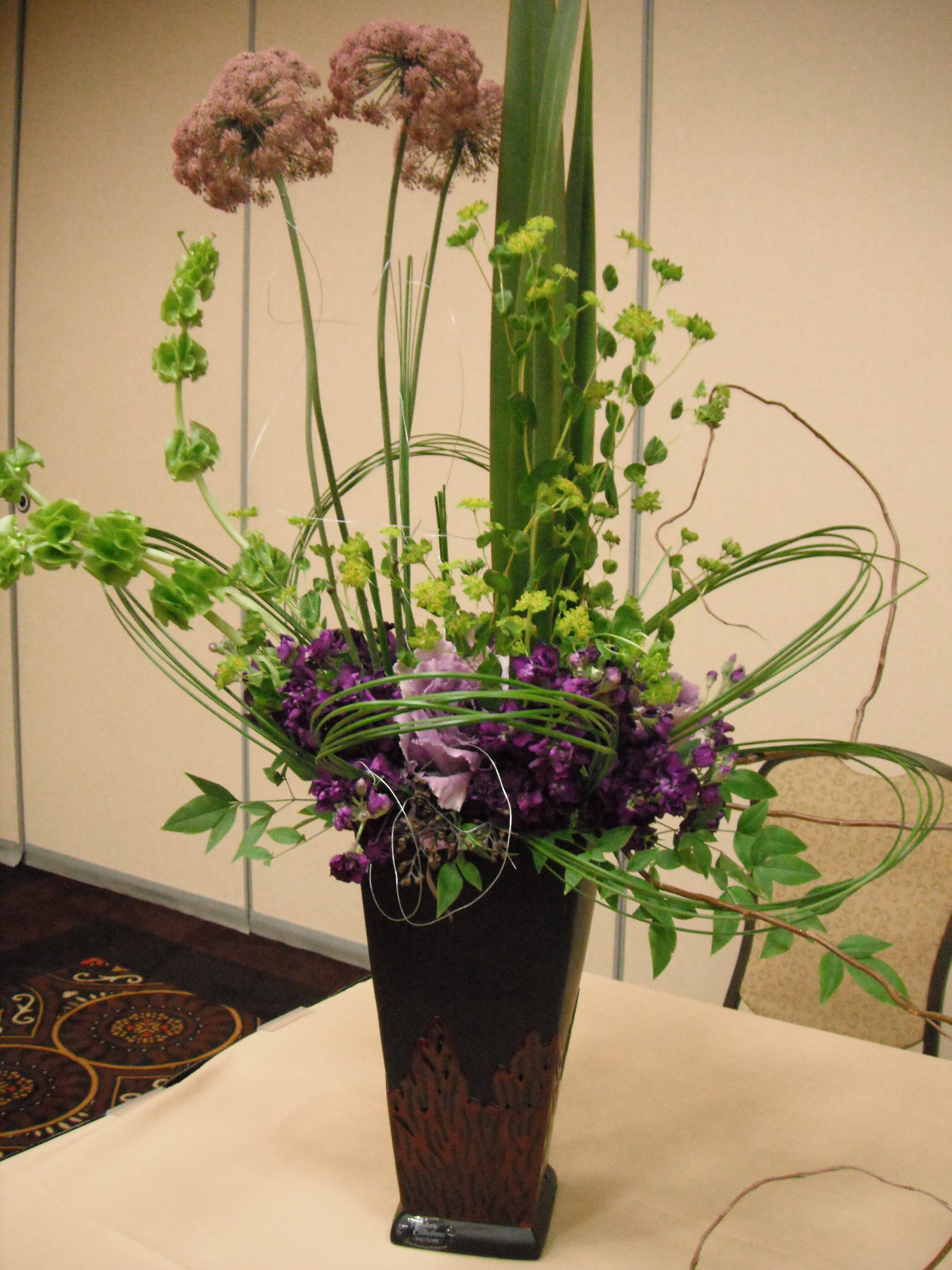 Tall purple and green floral arrangement in a black vase