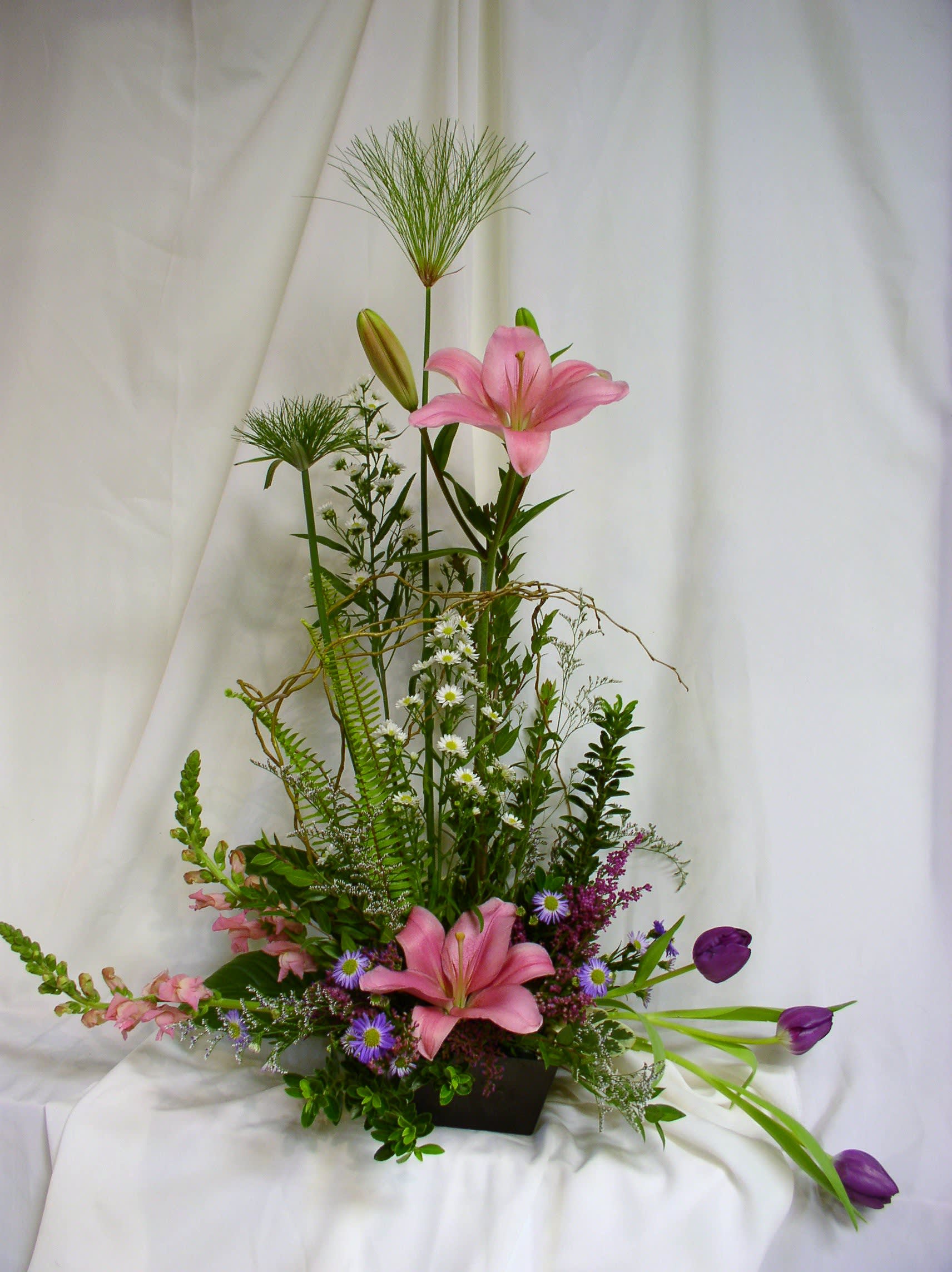 Tall floral arrangement with pink lilies and purple tulips in a dark container