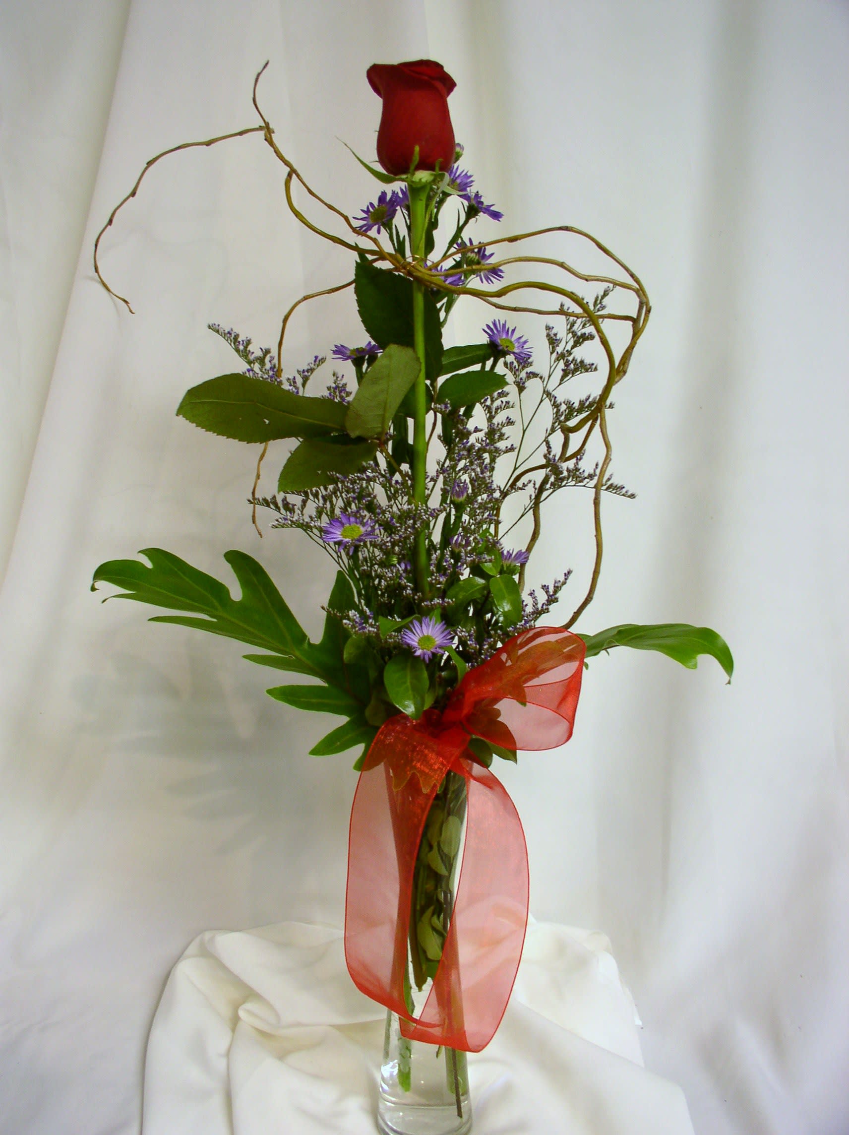 Tall red rose arrangement with purple filler flowers in a clear vase