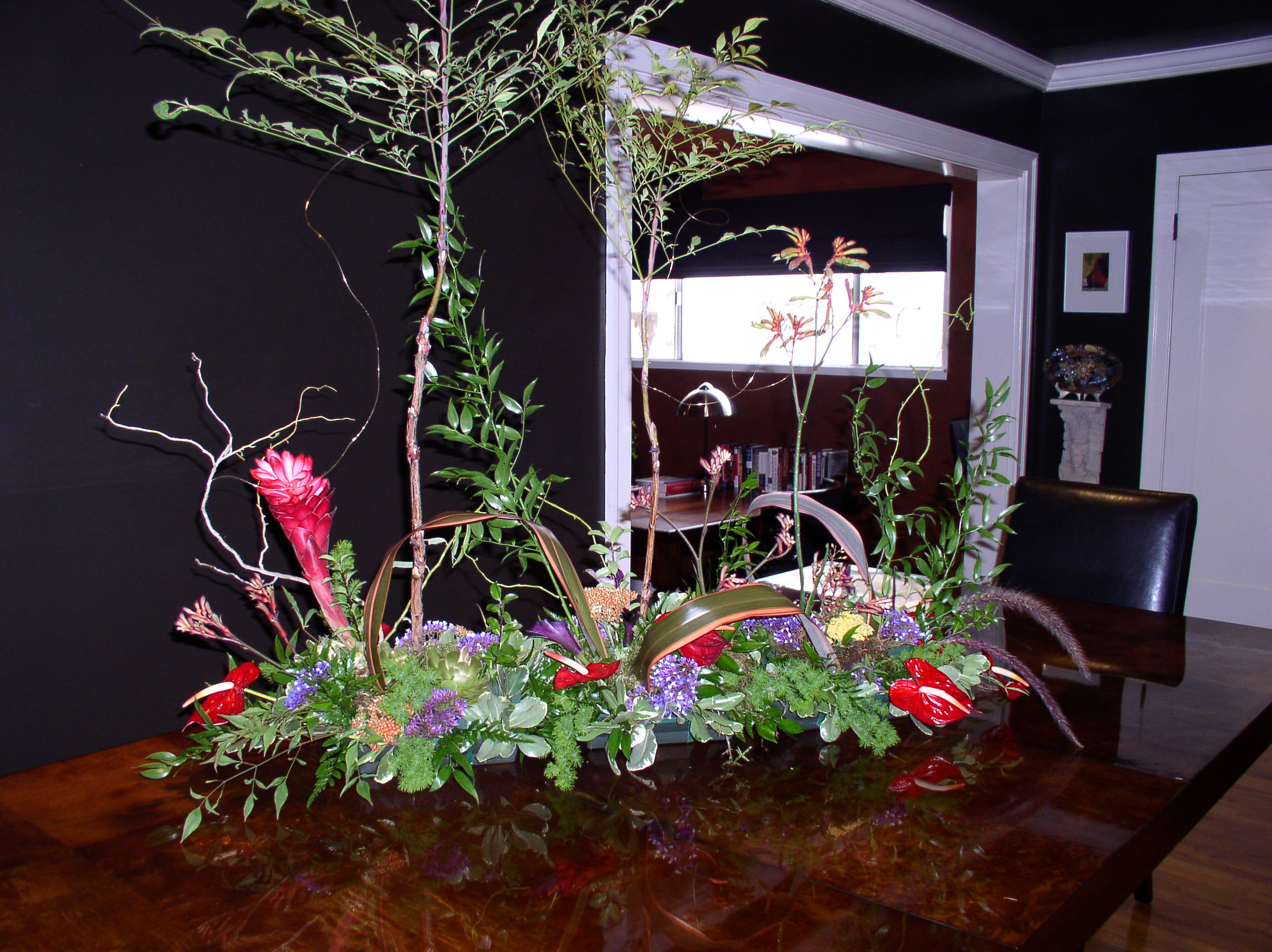 Large tropical floral centerpiece with red blooms and tall branches on a table