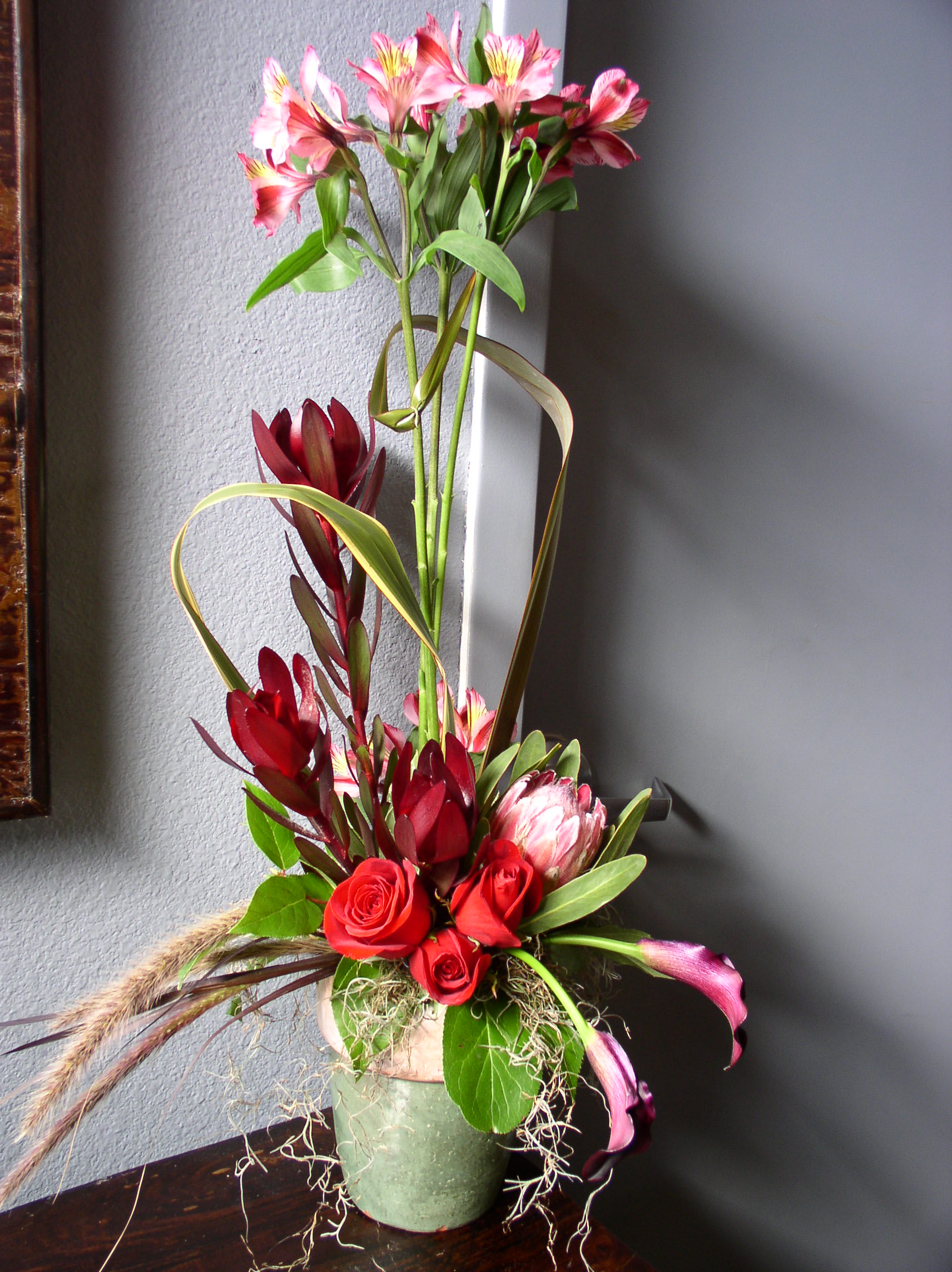 Tall floral arrangement with red roses and pink blooms in a green vase