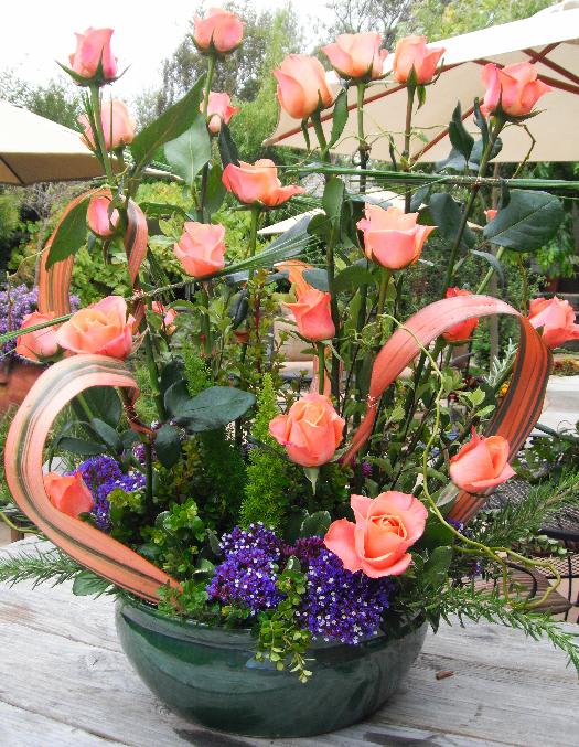 Tall arrangement of peach roses in a green bowl with ribbon loops