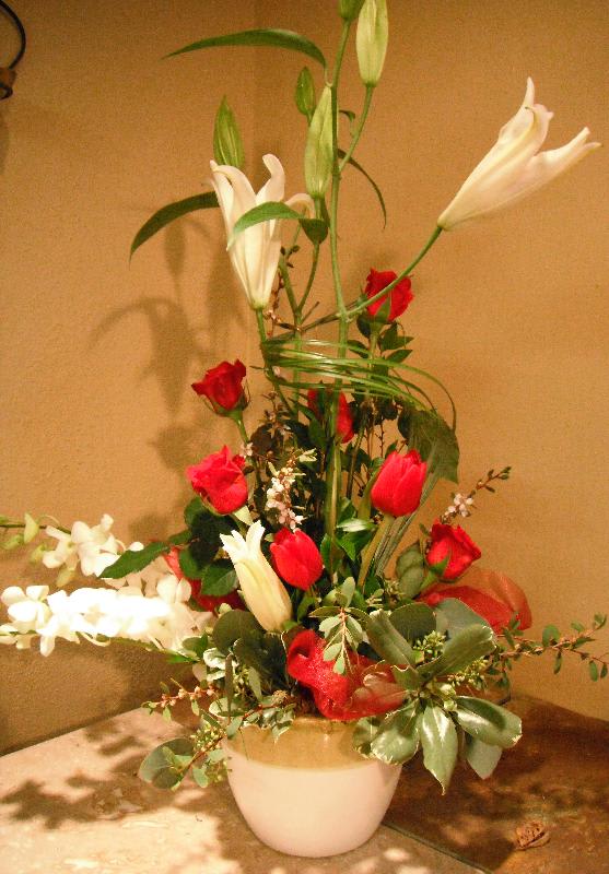 Tall floral arrangement with red roses and white lilies in a white vase