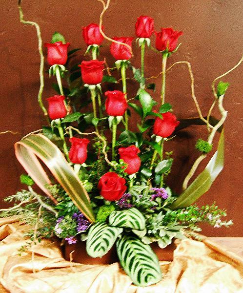 Tall arrangement of red roses with decorative foliage in a low container