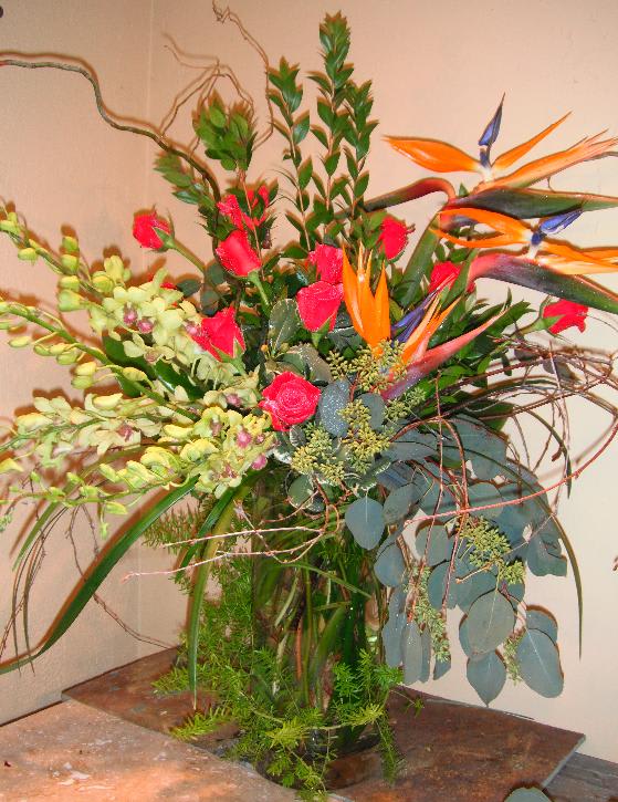 Tall tropical arrangement with orange bird-of-paradise and pink roses in a glass vase