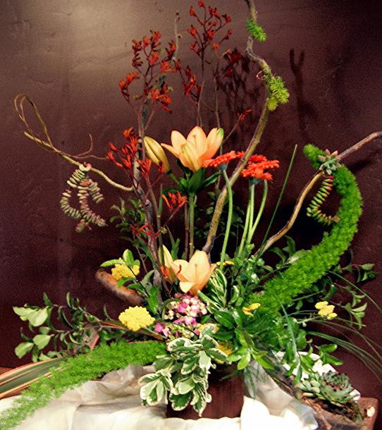 Tall floral arrangement with peach lilies and red-orange blooms