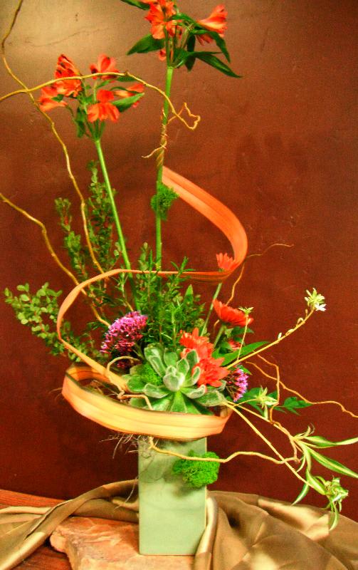 Tall floral arrangement with orange blooms in a square vase