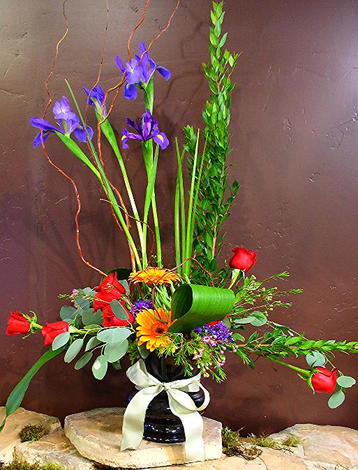 Tall mixed flower arrangement in a black vase with a white ribbon