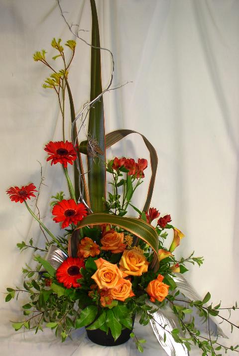 Tall floral arrangement with orange roses and red gerbera daisies in a black vase