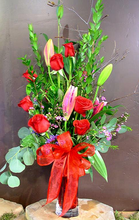 Tall bouquet of red roses and pink lilies in a glass vase with a red ribbon
