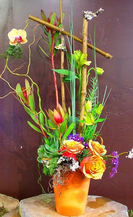Tall tropical floral arrangement in an orange vase with orchids and roses