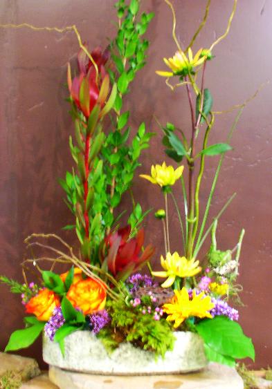 Tall mixed floral arrangement with yellow and orange blooms in a low container