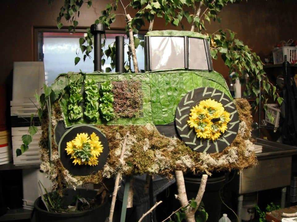 Green tractor-shaped floral display with yellow flower wheels