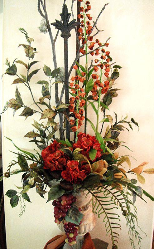 Tall floral arrangement with red blooms and orange spray flowers in a vase