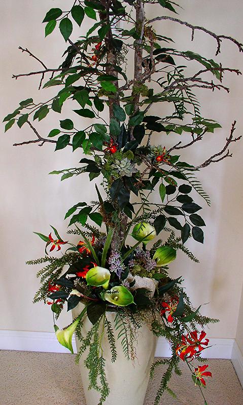 Tall floral arrangement with branches, red blooms, and green calla lilies in a white vase