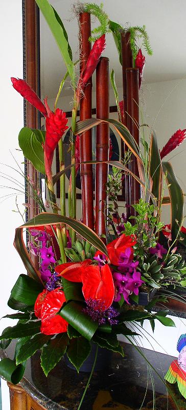 Tropical floral arrangement with red and purple blooms in a dark vase