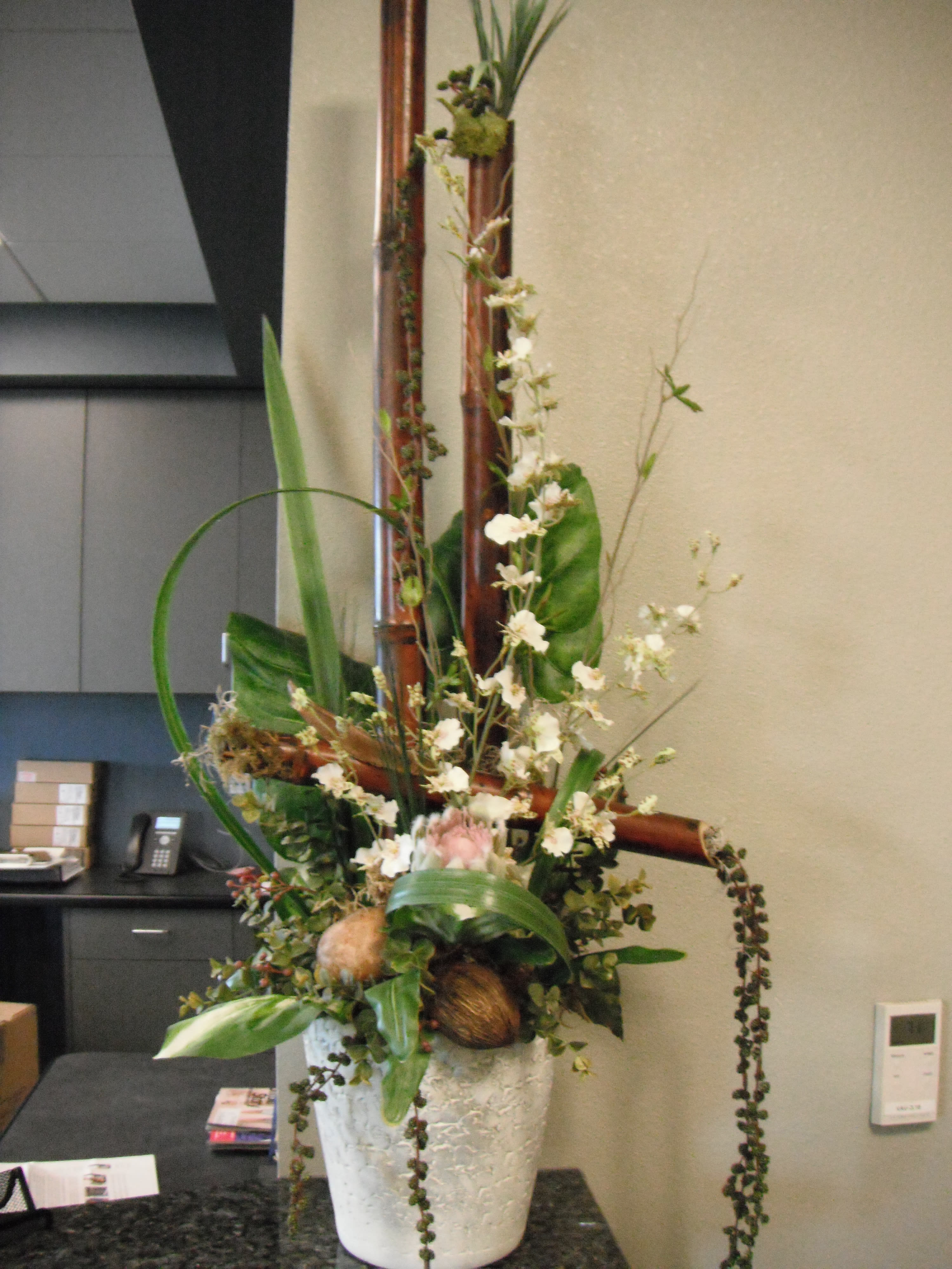 Tall floral arrangement in a white textured pot with white blossoms and greenery