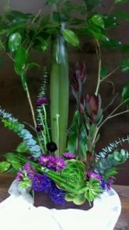 Tall tropical floral arrangement with purple blooms in a white container