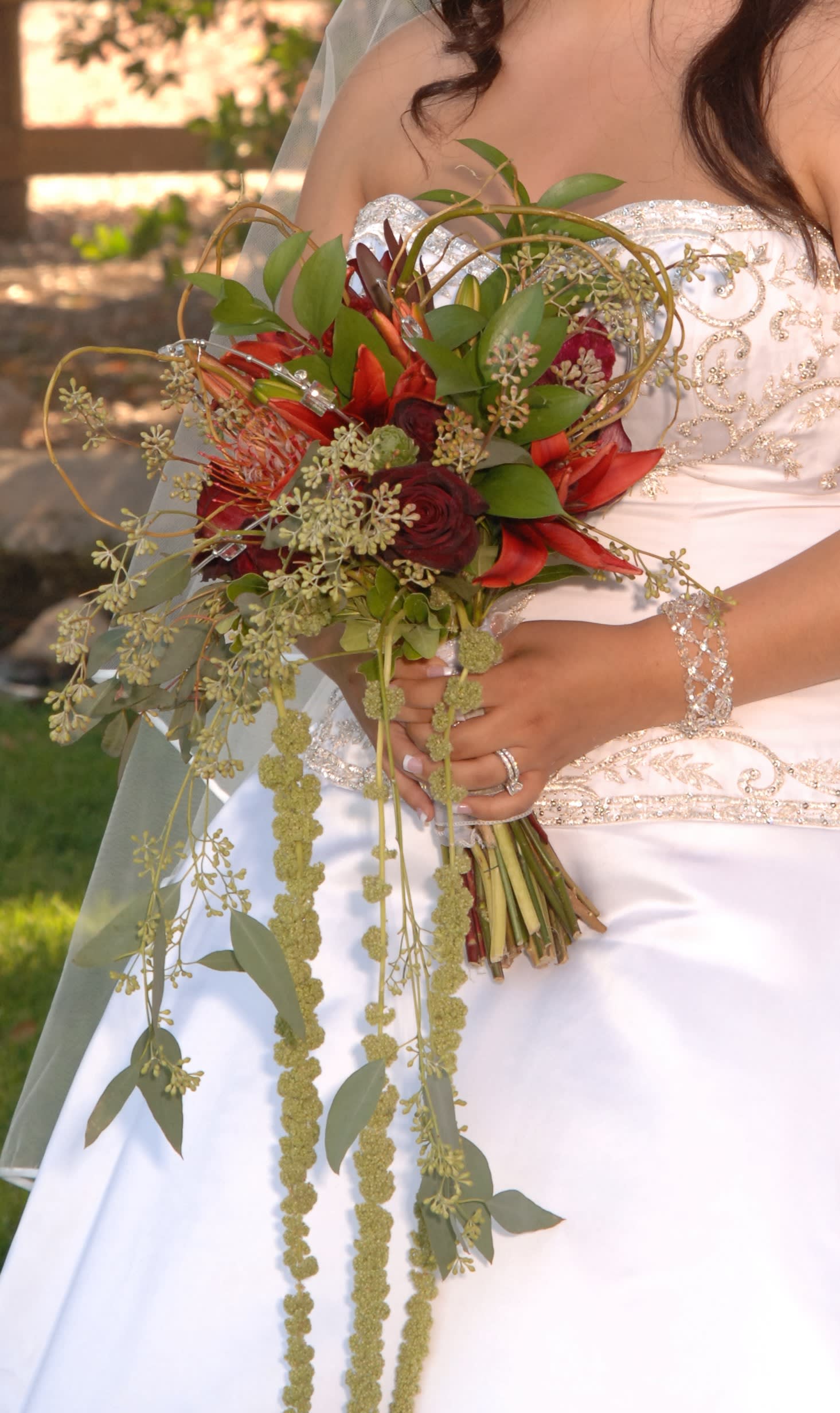 Bride holding a cascading bouquet of red flowers and greenery