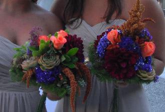Two bridesmaids hold colorful bouquets with succulents and orange blooms.