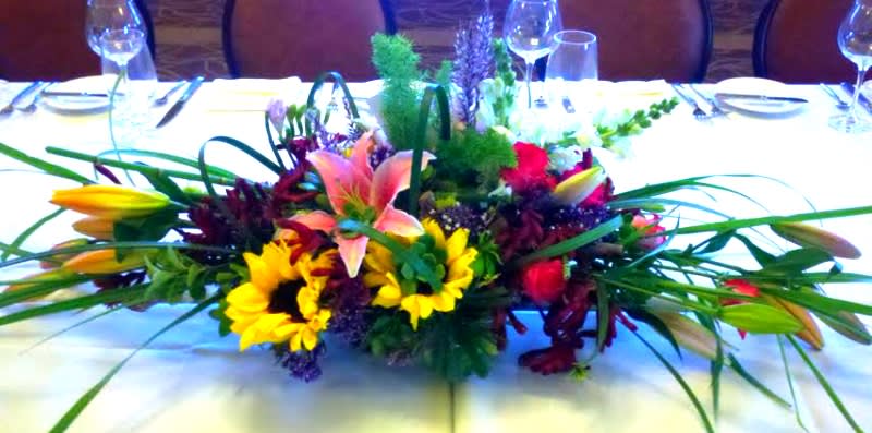 Low centerpiece with lilies, sunflowers, and roses on a banquet table