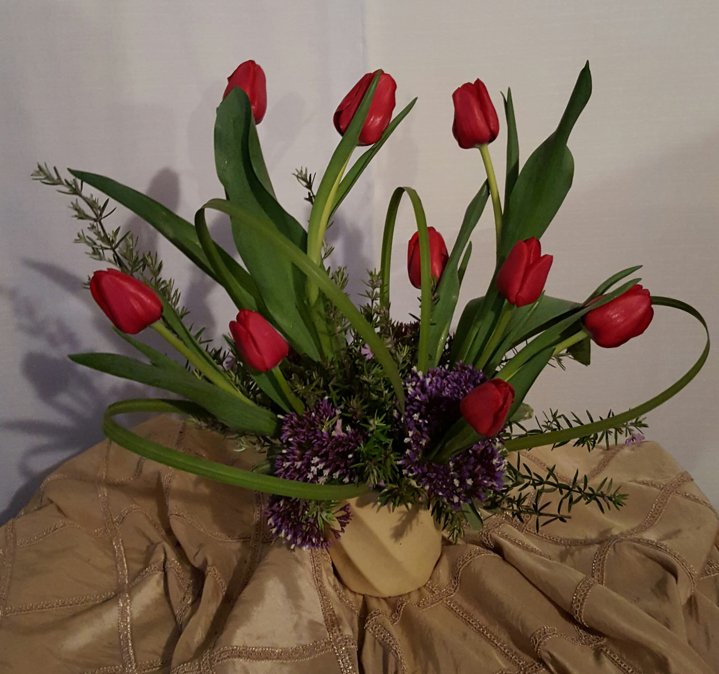 Red tulips arranged in a beige vase with purple filler flowers