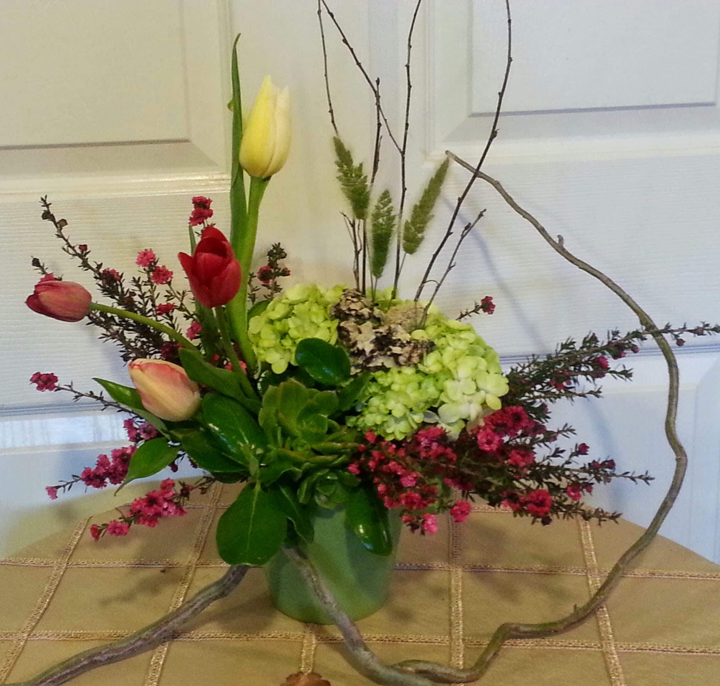Mixed tulips and hydrangeas in a glass vase with curly branches